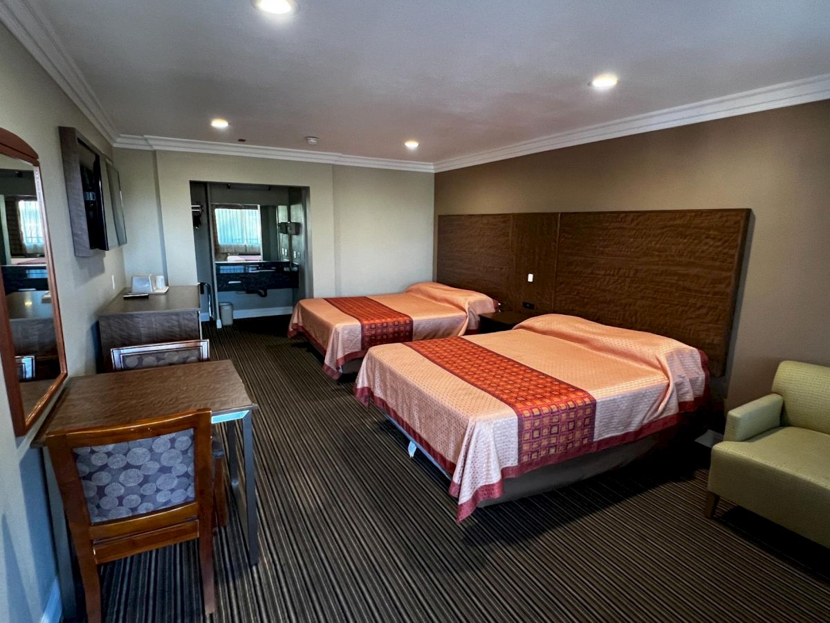 The image shows a hotel room with two beds, a chair, a desk, a wall-mounted TV, and a mirror, creating a cozy and functional space.