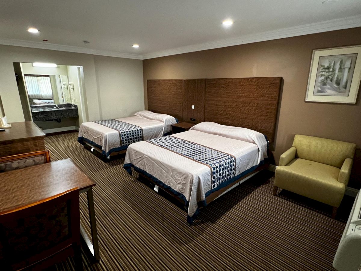 The image shows a hotel room with two double beds, a desk, a chair, a painting on the wall, and an air conditioner.