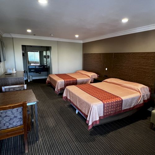 The image shows a hotel room with two beds, a mirror, desk, chair, TV, and an armchair, featuring neutral tones and modern decor.