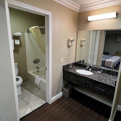 The image shows a bathroom with a bathtub, toilet, and sink. There's a large mirror above the sink and a light fixture.